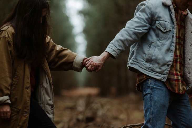 Pareja tomada de la mano por el bosque 