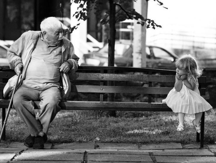 Niña sentada en una banca junto a su abuelo 