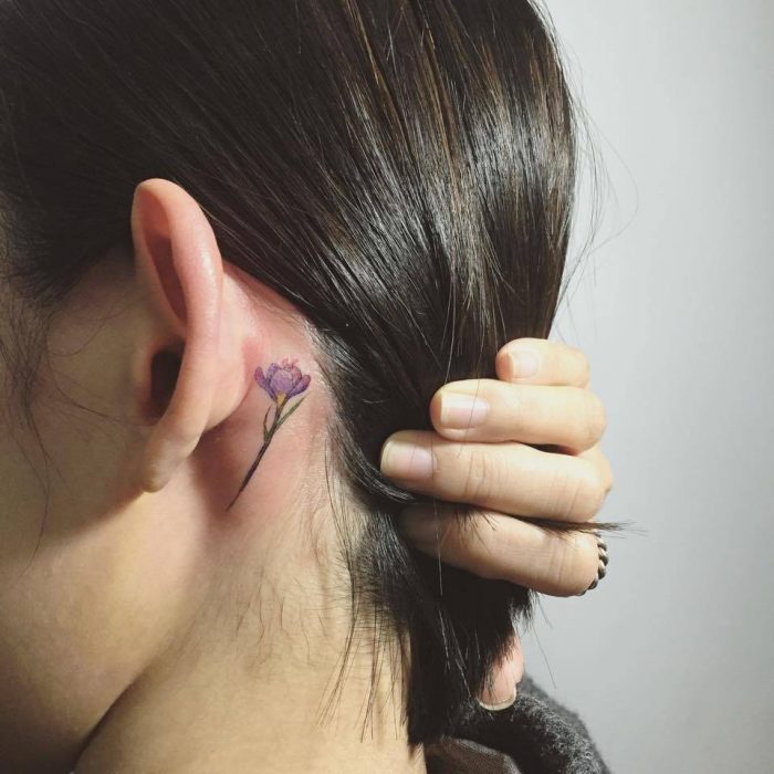 Chica con un tatuaje atrás de la oreja en forma de flor color morada