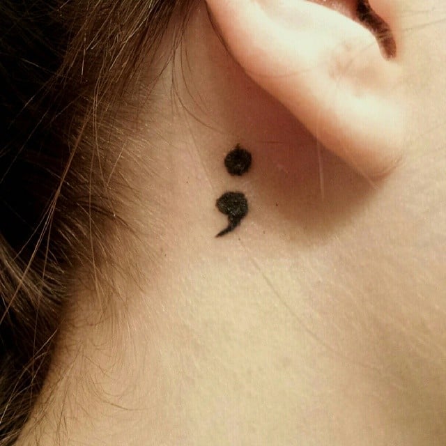 Chica con un tatuaje atrás de la oreja en forma de punto y coma