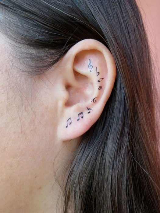 Chica con un tatuaje atrás de la oreja en forma de letras musicales 