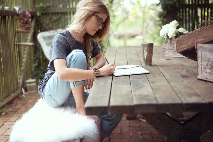 Chica sentada frente a una mesa escribiendo en una libreta 