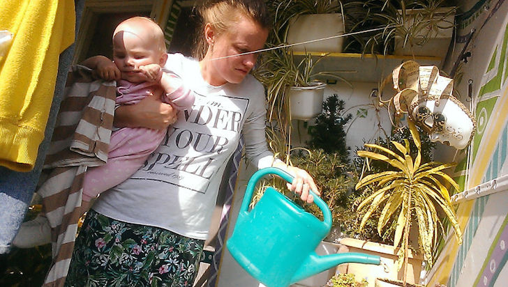 madre regando las plantas y cargando a su bebe