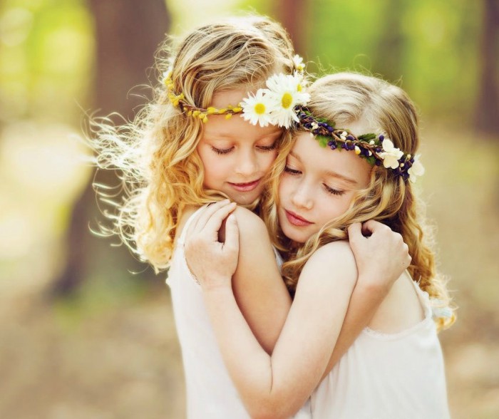 dos niñas rubias con diademas de flores abrazandose 