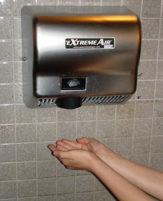 mujer calentándose las manos en secador de manos de aire