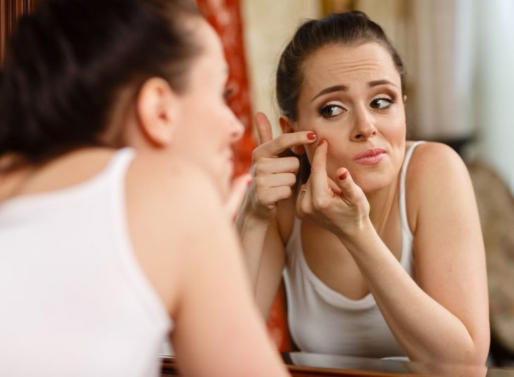 mujer exprimiendo un barro de la cara