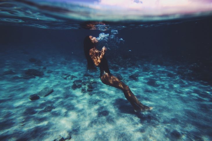 Chica en el fondo de una piscina nadando 