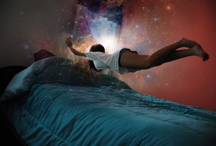 Chica flotando sobre su cama mientras ve una galaxia