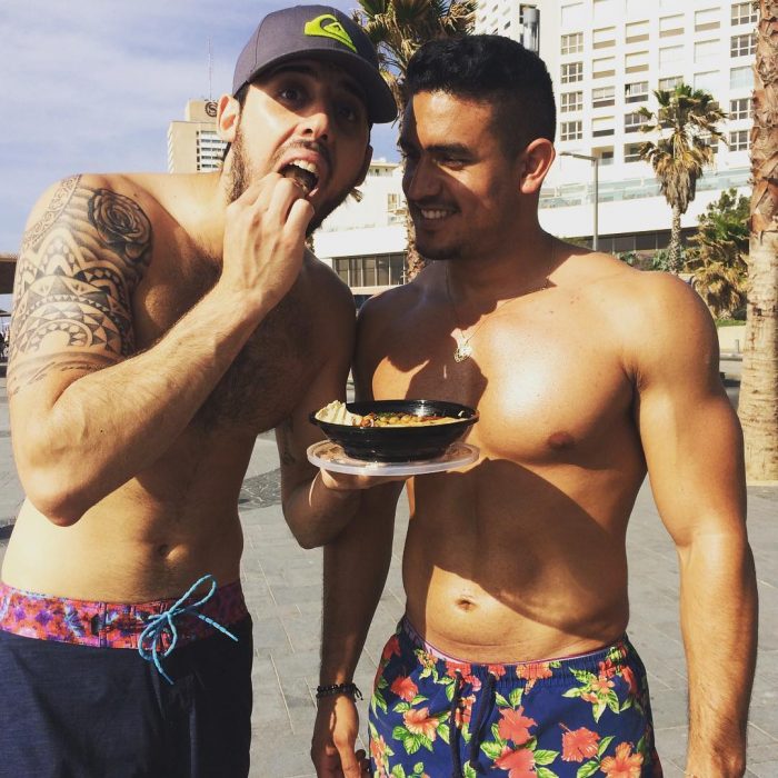 hombres en la playa sin playera comiendo 