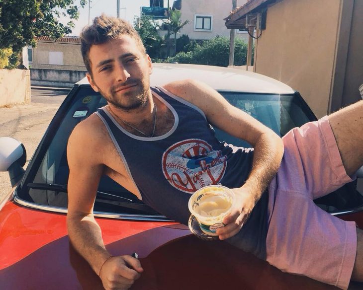 hombre sentado en cofre de coche comiendo algo 