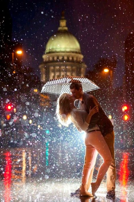 pareja dandose un beso bajo la lluvia y sombrilla