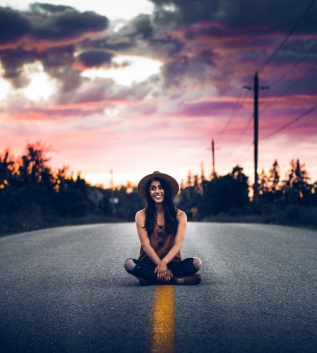 Chica sentada al centro de una autopista sonriendo