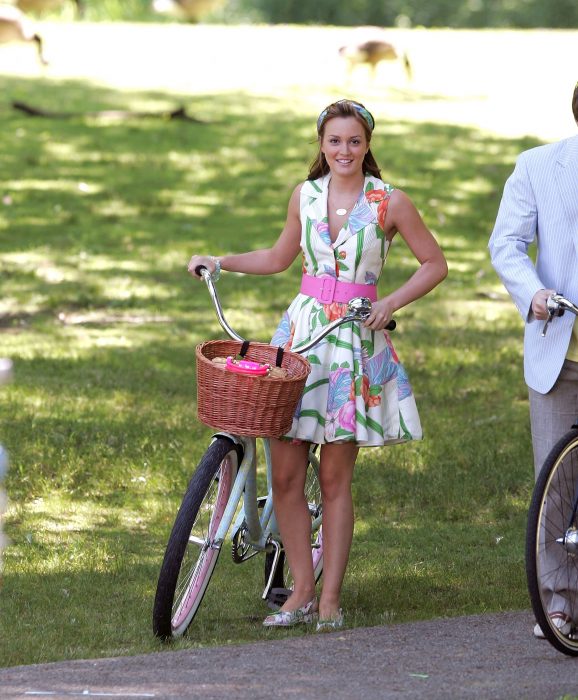 Blair Waldorf usando un vestido floreado con un cinturón rosa mientras sujeta una bicicleta 