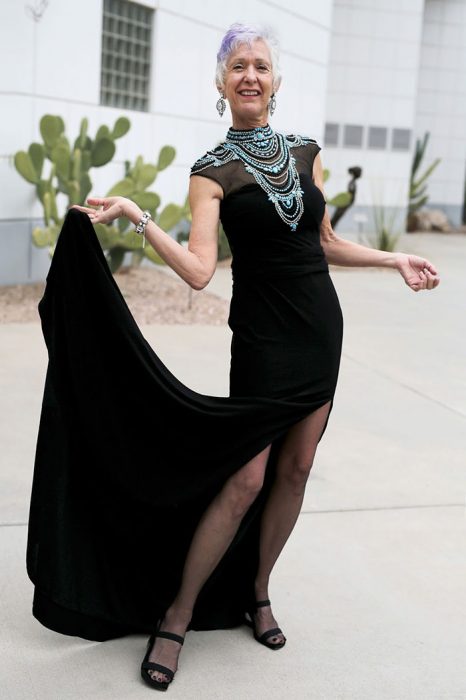 Mujer usando un vestido en color negro con medias y tacones negros y collares en color azul turquesa 
