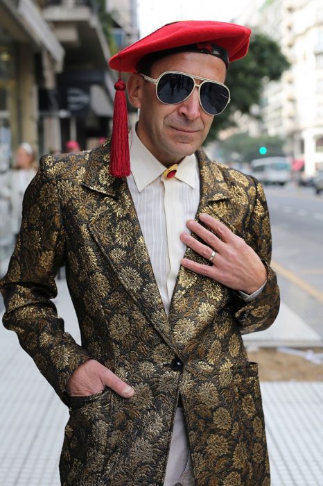 Hombre mayor usando un sombrero rojo y un saco en color dorado