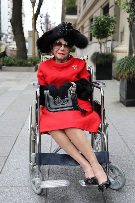 Mujer mayor en silla de ruedas usando un vestido rojo y una bolsa chanel 