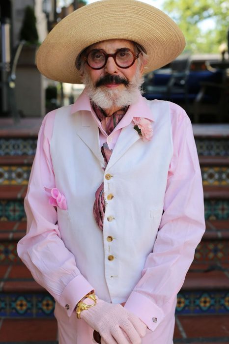 Hombre mayor usando una blusa color rosa y un chaleco en color blanco