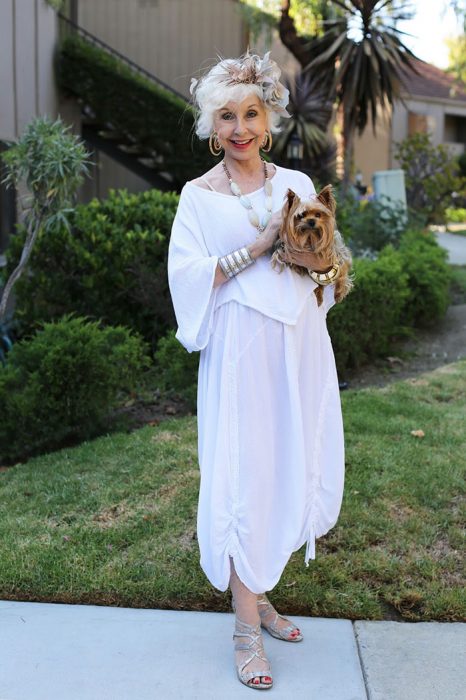 Mujer mayor usando un traje en color blanco y sosteniendo un perro 