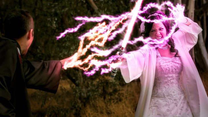 Pareja de novios peleando con sables de luz el día de su boda inspirada en Star Wars 