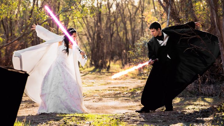 Pareja de novios peleando con sables de luz el día de su boda inspirada en Star Wars 