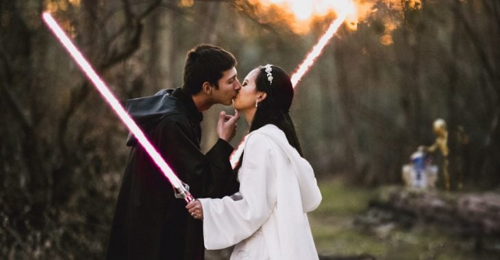Pareja de novios besándose mientras sostienen sables de luz el día de su boda inspirada en star wars 