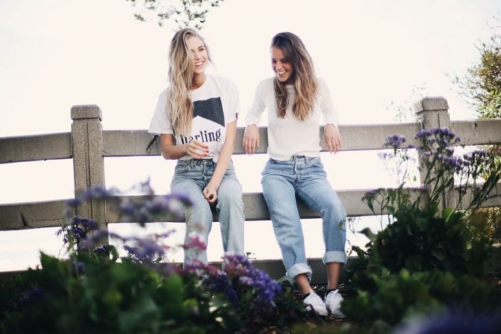 Chicas sentadas en una cerca conversando y riendo 