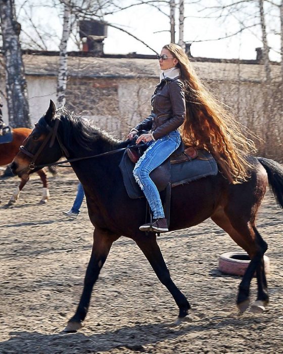 Chica con el cabello hasta los tobillos paseando en caballo 