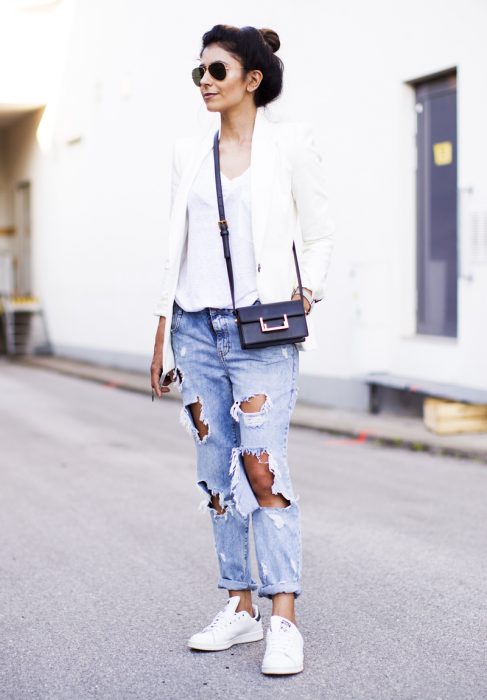 Chica usando pantalones en color azul rasgados, blazer y zapatillas en color blanco 