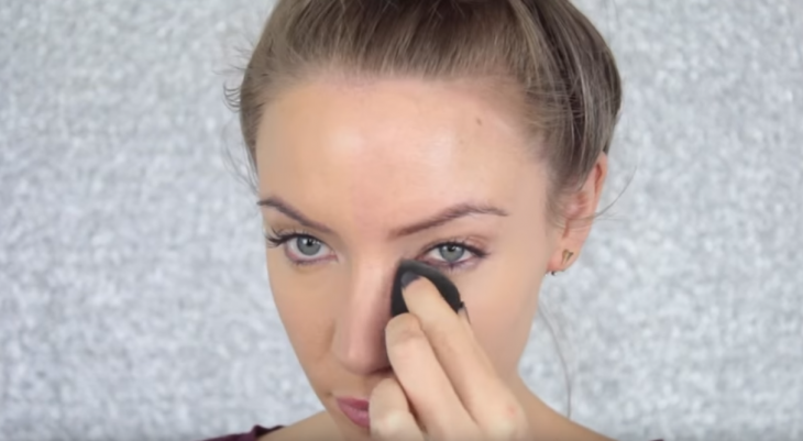 mujer rubia aplicando maquillaje en ojeras 