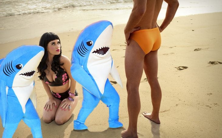 mujer sentada en la playa con hombre en frente y tiburones 