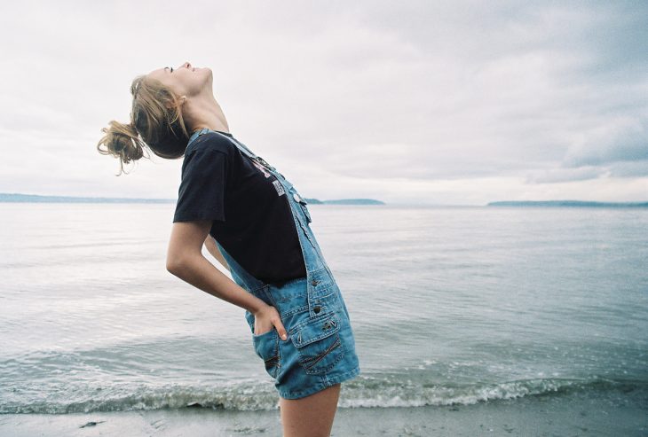 Chica mirando hacia el cielo frente al mar 