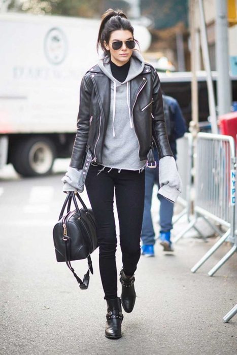 Chica usando hoddies y blazer en color negro y gris mientras camina por la calle 
