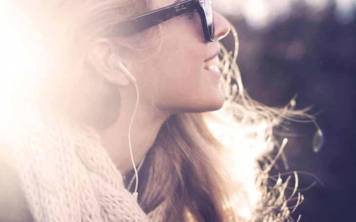 Mujer de perfil sonriendo y escuchando música con audífonos