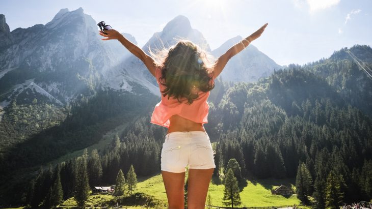 Mujer de espaldas con los brazos abiertos con un paisaje de montañas y árboles