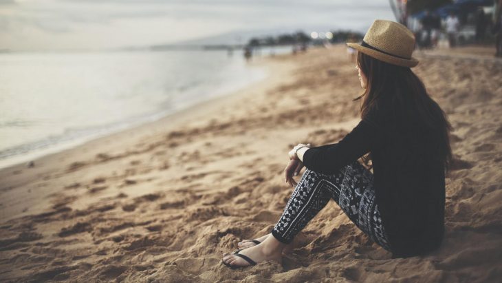 Mujer sentada en la arena viendo el atardecer en la playa