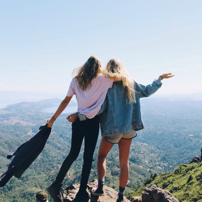 Chicas paradas sobre una montaña viendo hacia el vacío 
