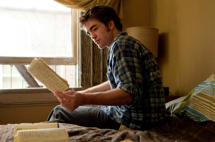 Robert Pattinson leyendo unas hojas que están sobre una cama en la película remember me 