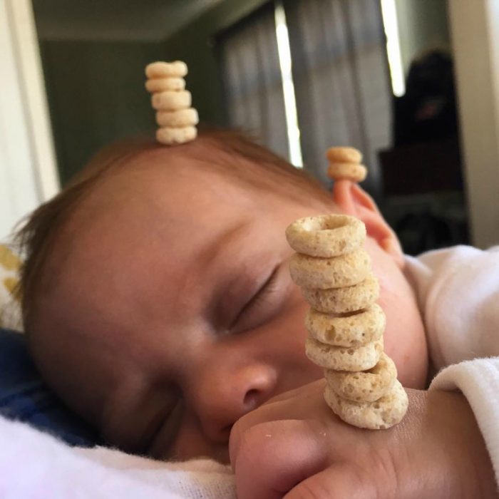 pequeño bebé en brazos dormido con pila de cereal en su frente