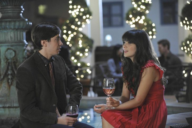 Escena de la serie new girl. Chica conversando con un chico mientras toman vino 