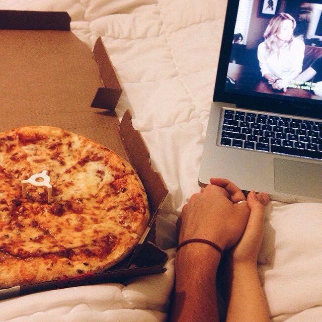 pareja tomados de la mano con pizza y computadora en cama