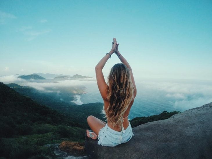 Chica sentada en el filo de una montaña haciendo posiciones de yoga 
