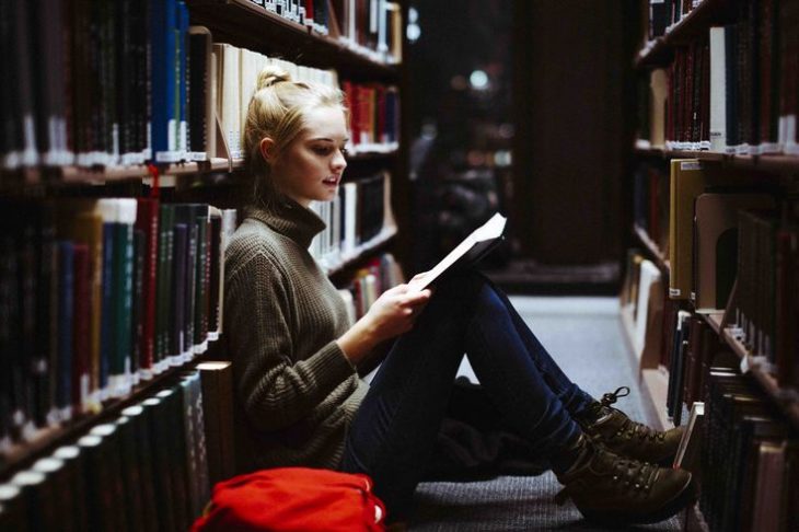Chica sentada sobre una estantería de libros en la biblioteca 