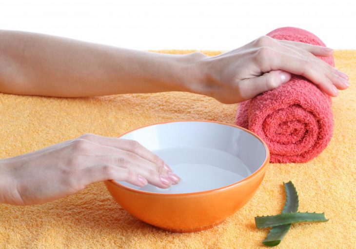 Chica sumergiendo sus uñas en agua caliente para iniciar con una manicura 