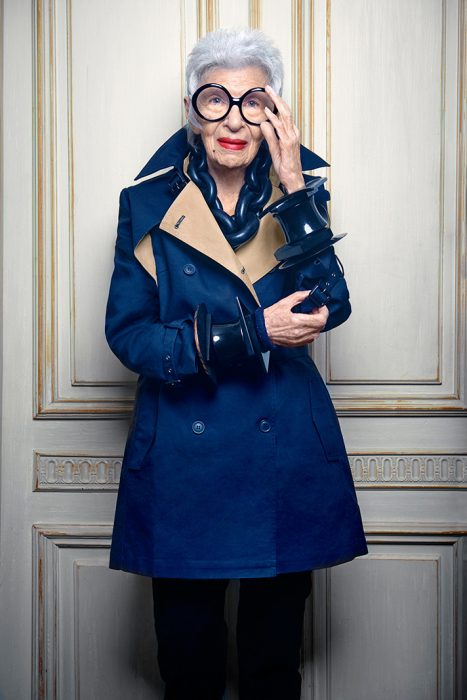 Iris Apfel usando una gabardina en color azul y cadenas extravagantes en color azul 