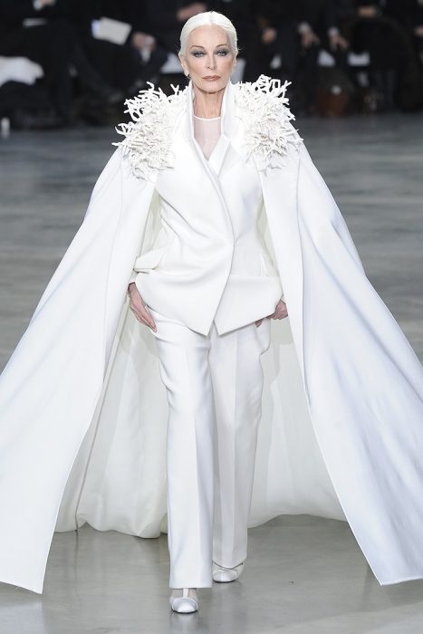 Carmen Dell’Orefice desfilando en una pasarela de modas minentras usa un traje sastre en color blanco con capa 