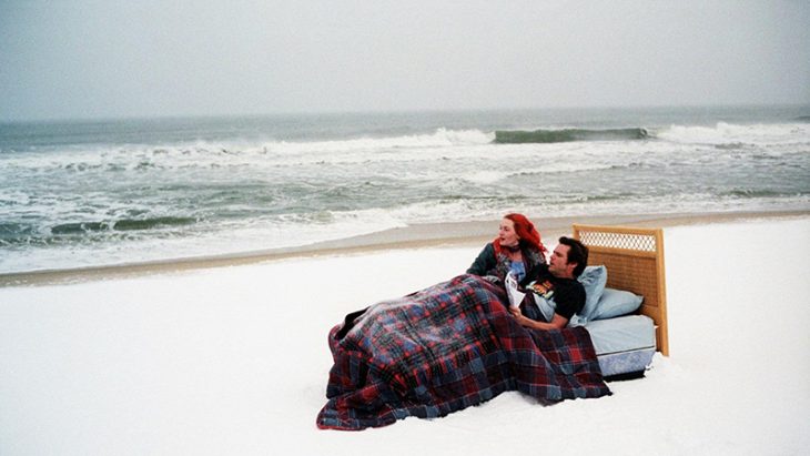 hombre en la cama con mujer de cabello rojo en medio del mar y nieve 