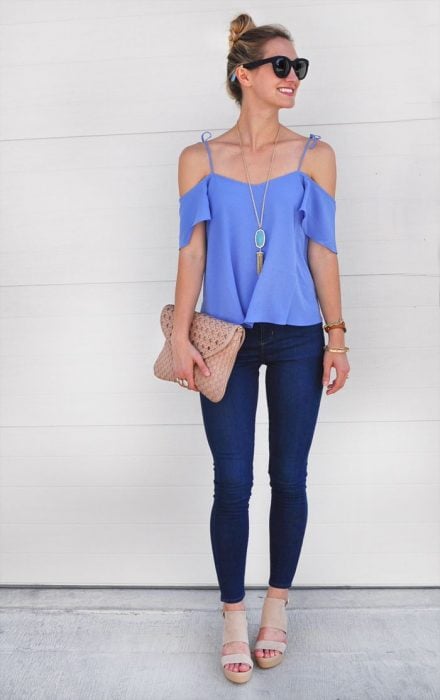 Chica usando una blusa sin hombros de color azul y pantalón de mezclilla, sosteniendo una bolsa tipo clutch de color café