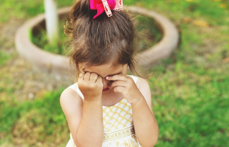 Niña llorando y tapando su rostro con sus manos 