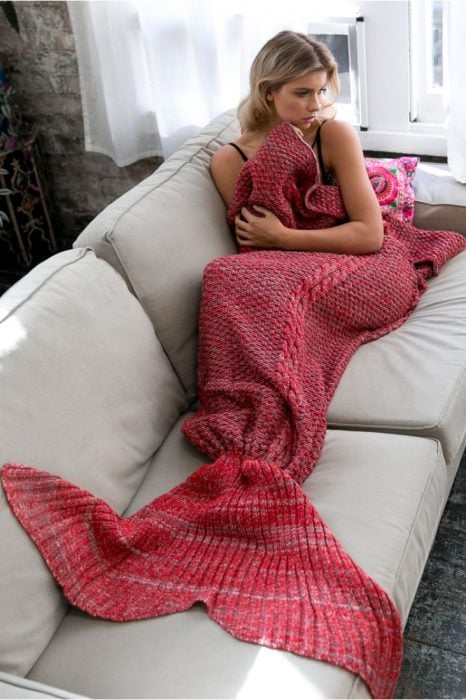 Chica recostada en un sofá mientras tiene las piernas cubiertas por una frazada cola de sirena 