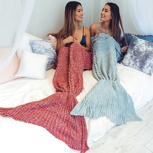 Chicas sentadas en una cama mientras tienen las piernas cubiertas por una frazada de cola de sirena 